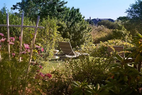 A serene garden scene with lounge chairs, lush greenery, and a clear blue sky in the background.