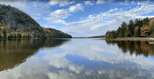 Vibrant autumn trees and blue sky reflected in the calm waters of Echo Lake in Maine during the fall.