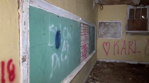 An abandoned room with chalkboards and graffiti on the walls, showing signs of neglect and decay.