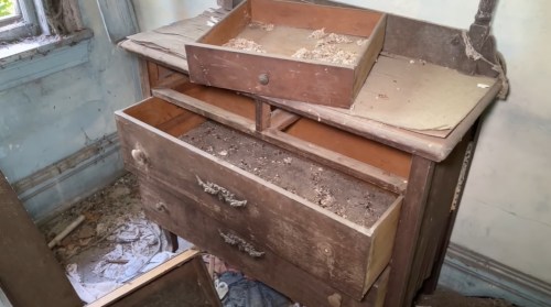 An old, dusty dresser with open drawers, showing debris and neglect in a dimly lit room.