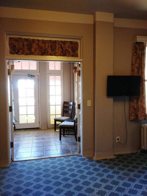 Interior view of a room with a doorway leading to a bright area, a chair, and a wall-mounted TV.