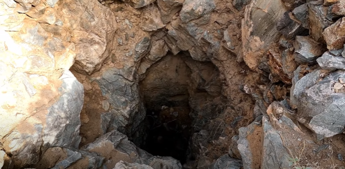 A deep, rocky mine shaft surrounded by rough stone walls and loose dirt.