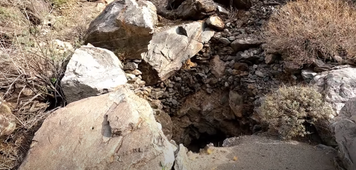 A rocky landscape with large boulders and sparse vegetation, revealing a deep crevice in the ground.