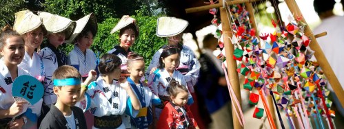 A group of people in traditional Japanese attire, smiling and standing near colorful decorations at a festival.