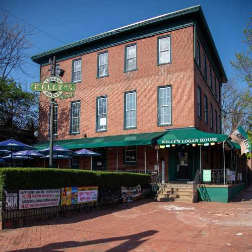 A brick building with green awnings, featuring outdoor seating and signage for Kelly's Logan House Cafe.