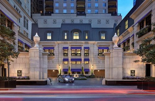 Elegant hotel entrance with stone pillars, modern architecture, and a sleek car parked in front, illuminated at dusk.