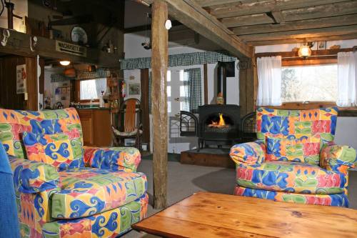 Cozy living room with colorful patterned chairs, a wooden table, and a fireplace surrounded by rustic wooden beams.