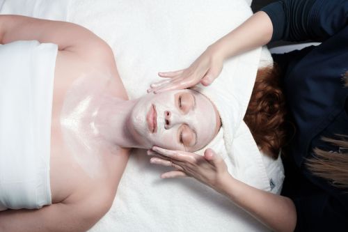 A person receiving a facial treatment, with a mask on their face and a therapist gently applying product.