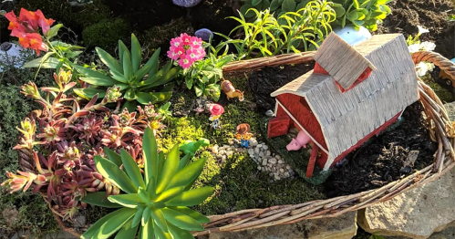 A miniature farm scene with a red barn, tiny figures, and colorful flowers in a woven basket garden.