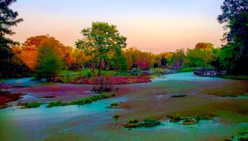 A serene landscape featuring a calm, muddy waterway surrounded by lush trees and colorful foliage at sunset.