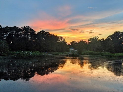 A serene sunset over a calm lake, reflecting vibrant colors and surrounded by lush trees.