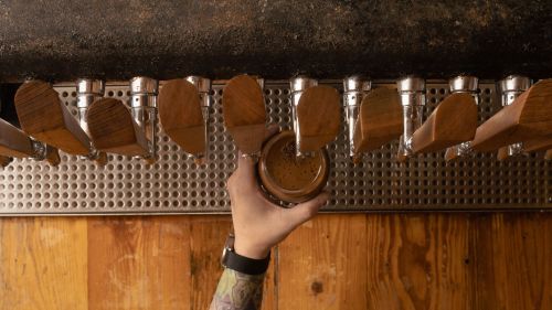 A hand holds a glass under a row of wooden beer taps at a bar, with a rustic wooden counter below.