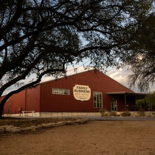 A rustic red building with a sign reading "Family Business Beer Company" surrounded by trees and a gravel area.