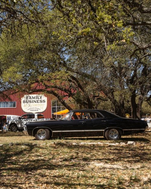 A classic black car parked near a red barn with a "Family Business" sign, surrounded by trees and autumn leaves.