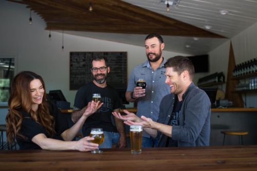A group of four friends enjoying drinks at a bar, laughing and chatting around a wooden table.