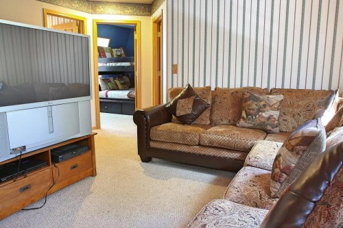 Cozy living room with a large TV, patterned sofas, and a view of a bedroom with bunk beds in the background.