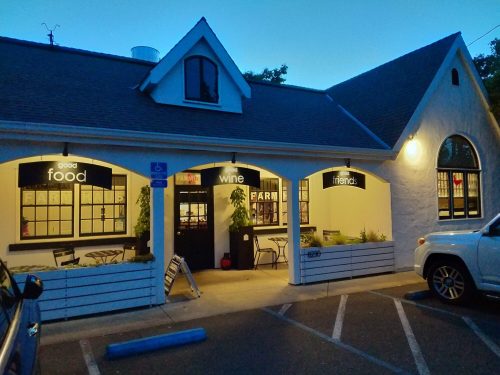 Exterior of a cozy restaurant with signs for "food," "wine," and "friends," illuminated at dusk.