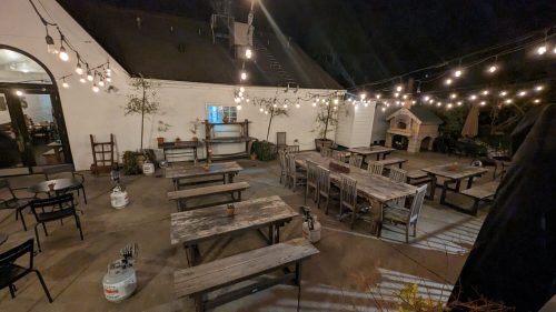 Outdoor dining area at night, featuring wooden tables, string lights, and a cozy atmosphere.