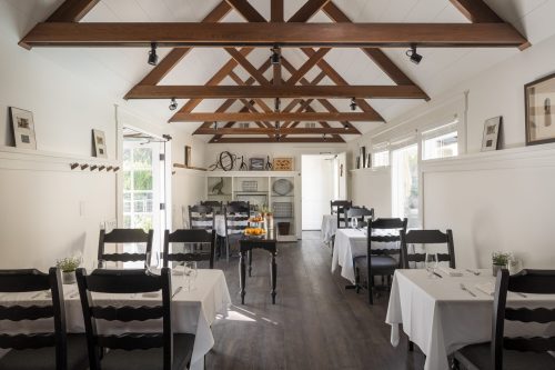 A bright, airy restaurant interior with wooden beams, white tables, and a cozy atmosphere.