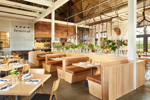 Modern restaurant interior with wooden booths, tables, and greenery, featuring a bright, open atmosphere.