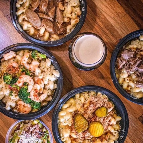 A variety of pasta dishes with shrimp, beef, and vegetables, served in black bowls alongside a drink.