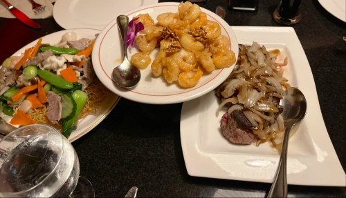 A table with three dishes: stir-fried vegetables with meat, crispy shrimp, and a beef dish with onions.