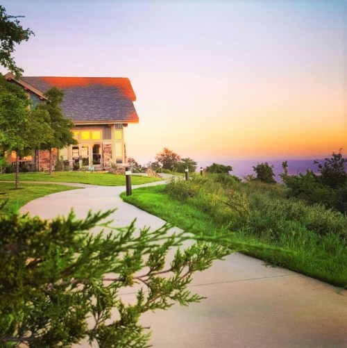 A scenic view of a house at sunset, with a winding path and lush greenery leading to the horizon.