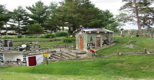 A unique, mosaic-covered building surrounded by greenery and decorative landscaping in a serene outdoor setting.
