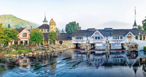 A picturesque estate with unique architecture, surrounded by lush greenery and reflecting in a calm body of water.