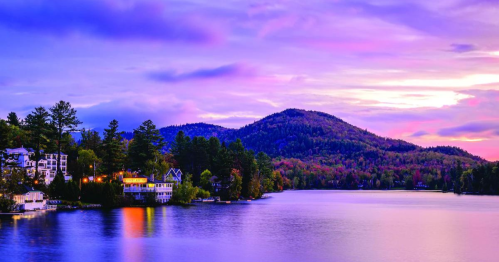 A serene lake at sunset, surrounded by mountains and colorful trees, with charming houses along the shore.