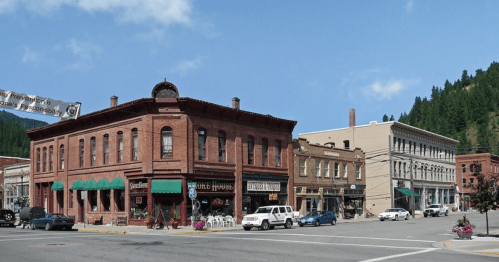 Historic brick buildings line a street in a small town, with shops and greenery under a clear blue sky.