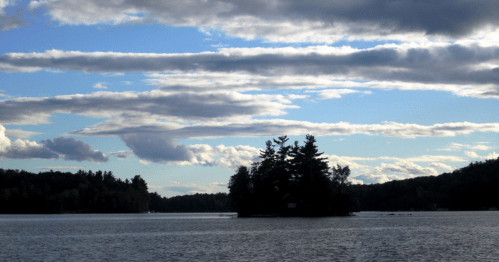 A serene lake scene with an island surrounded by trees under a cloudy sky.