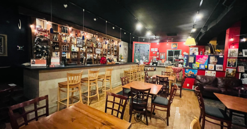 Cozy bar interior with wooden tables, chairs, and a well-stocked counter, featuring colorful decor and warm lighting.