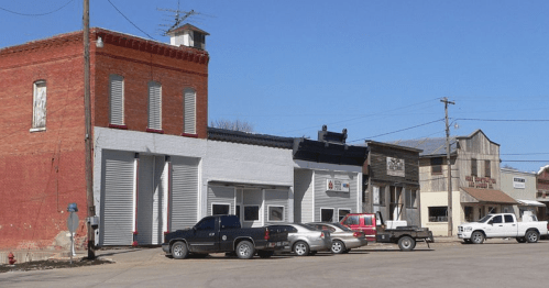 A row of buildings with various storefronts and parked trucks on a clear day.