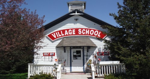 A quaint white building with a red sign reading "Village School," featuring a gift shop and surrounded by greenery.