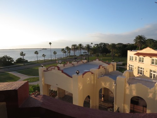View of a waterfront with palm trees, a building, and a clear sky during sunset.