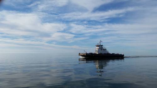 A tugboat glides across calm waters under a blue sky with wispy clouds.