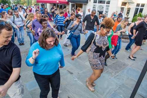 A diverse group of people dancing together outdoors, enjoying a lively event with smiles and energetic movements.