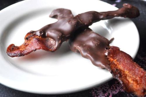 Chocolate-covered bacon strips on a white plate.