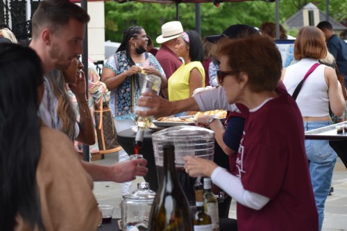 A lively outdoor event with people socializing and enjoying drinks at a bar table.