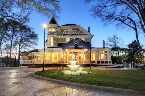 A charming hotel with a turret, illuminated at dusk, featuring a fountain and landscaped grounds.