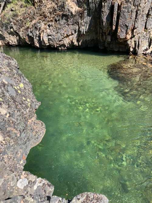 Clear green water in a rocky pool surrounded by rugged cliffs and natural vegetation.