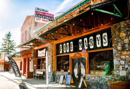 Exterior of Five Marys restaurant with a stone facade, signage for steaks, burgers, and cocktails, and flags displayed.