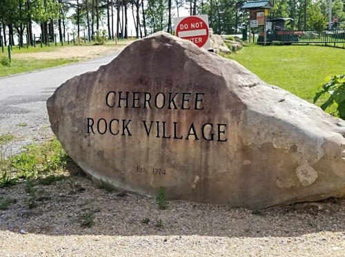 A large rock with "Cherokee Rock Village" and "Est. 1974" engraved, set in a grassy area near a park entrance.