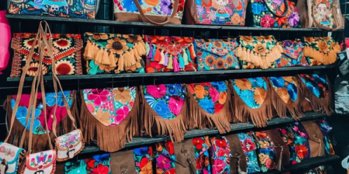 A vibrant display of colorful embroidered bags and purses with floral and fringe designs on wooden shelves.
