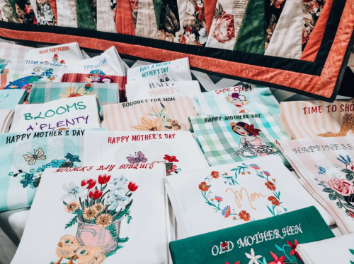 A colorful display of embroidered towels and fabric featuring Mother's Day themes and floral designs.