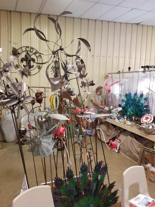 A vendor arranges colorful metal art and decorations at a craft fair, with various sculptures in the foreground.