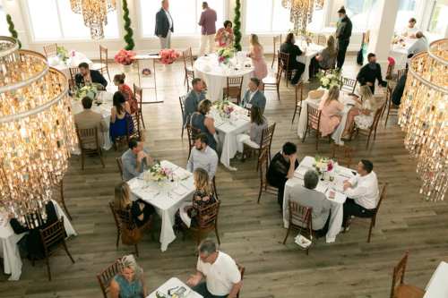 A spacious dining area with elegantly set tables, guests mingling, and chandeliers overhead.