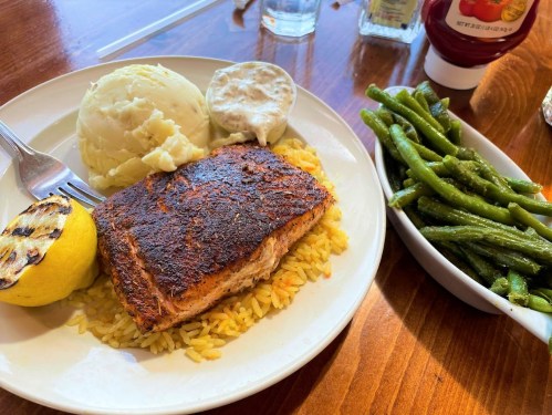 A plate with seasoned salmon, rice, mashed potatoes, a lemon wedge, and green beans on the side.
