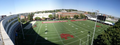 A panoramic view of a football field at Washington State University, featuring green turf and surrounding buildings.